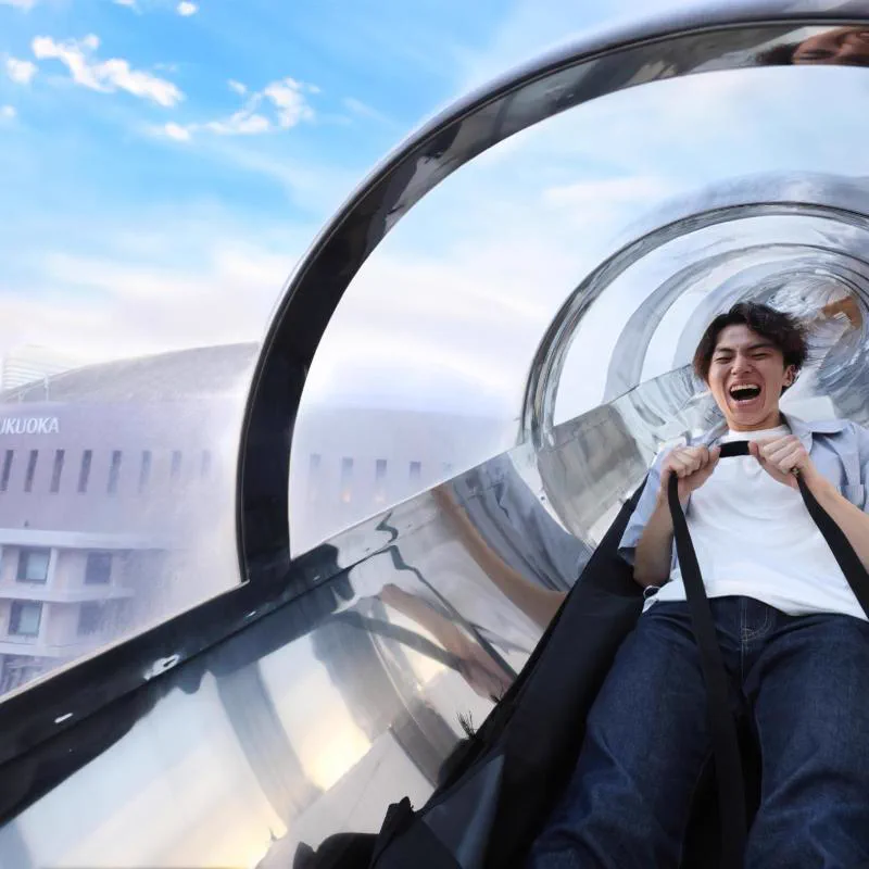 BOSS E・ZO FUKUOKA sube-ZO: a rider enters the transparent exterior tube slide from the rooftop level.