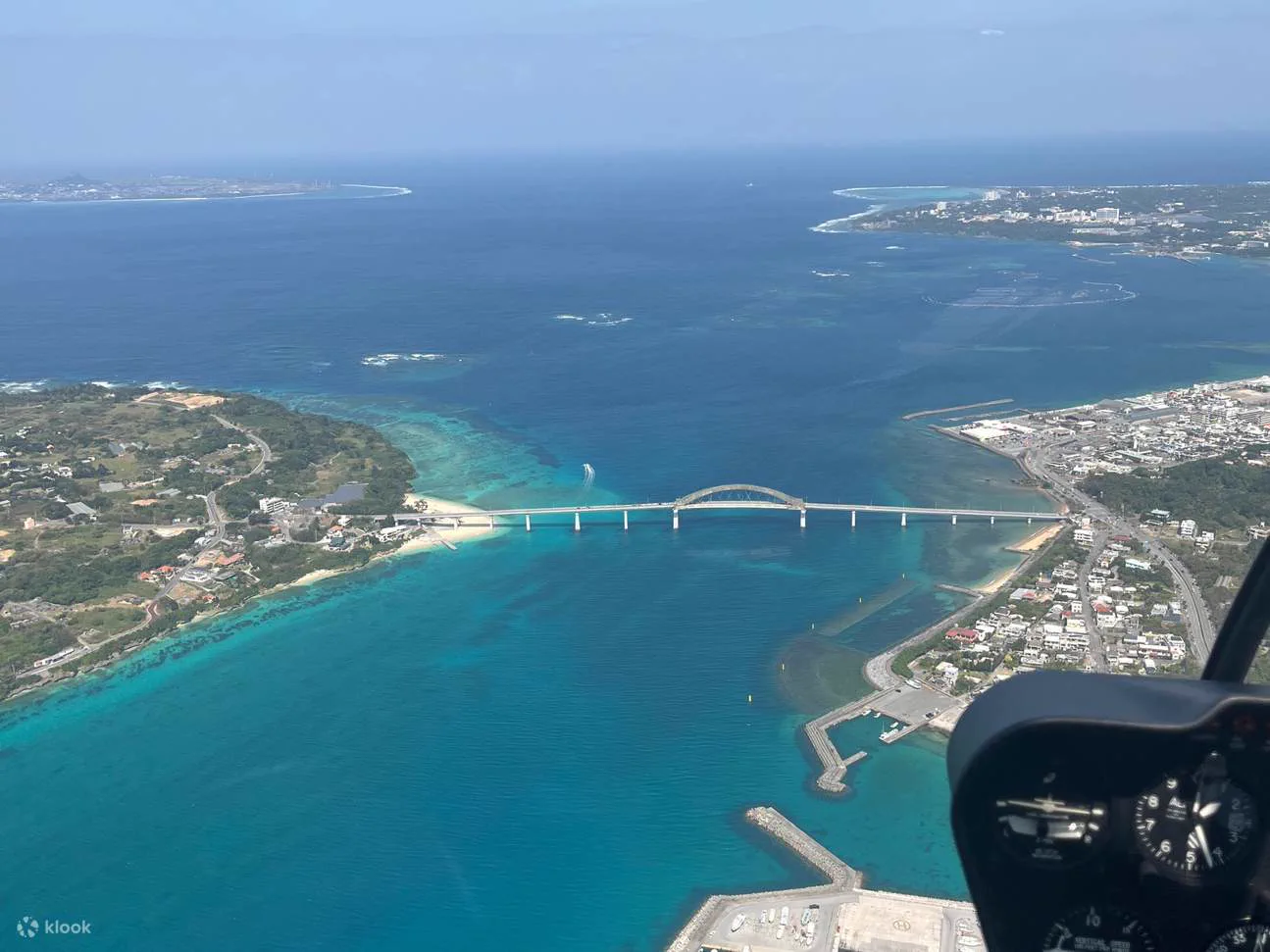 Okinawa coastline and bridge seen from a helicopter. The value of a longer flight is reaching Kouri Island or northern waters, not simply adding minutes.